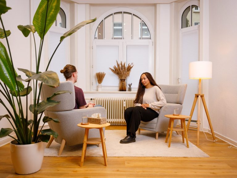 Therapieraum Zwei Personen sitzen sich in einem Therapieraum gegenüber. Eine Person spricht, während die andere Person zuhört.